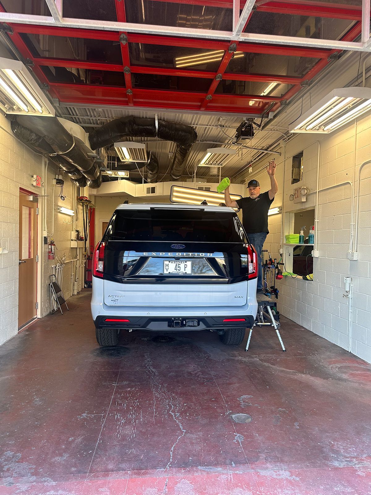 SUV being washed in a car wash bay, with a worker cleaning the ceiling overhead.