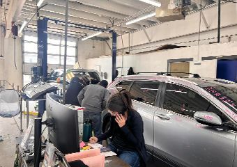 A woman is sitting in front of a car in a garage talking on a cell phone.
