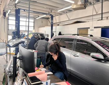 A woman is sitting at a desk in a car dealership talking on a cell phone.