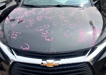 A black chevrolet cruze with hail damage on the hood.