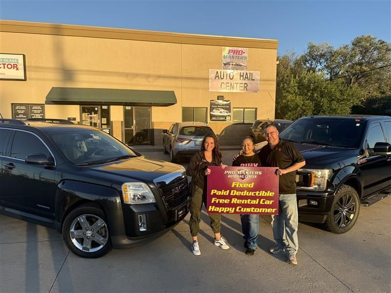 Two people holding a sale sign between two black SUVs outside an auto mall storefront