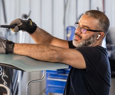 Man in gloves and glasses adjusting a car part in a garage or workshop