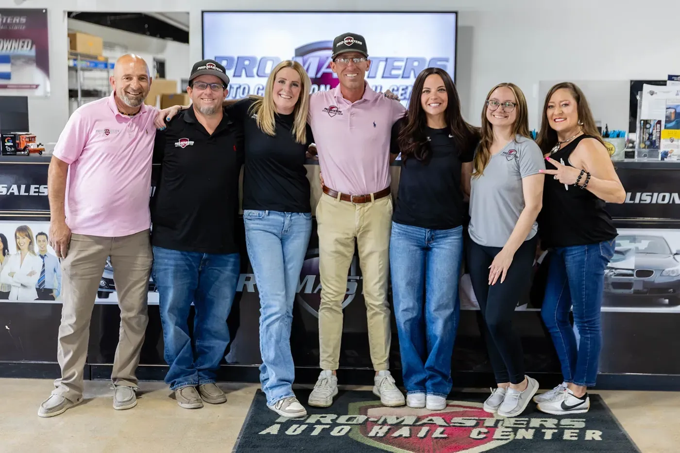Six smiling staff members posing in a tire shop showroom with an Auto Care Center sign behind them