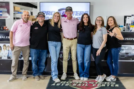 Six smiling staff members posing in a tire shop showroom with an Auto Care Center sign behind them