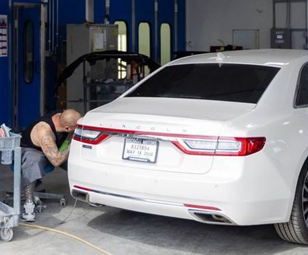 Mechanic working on the rear of a white sedan in an auto repair shop