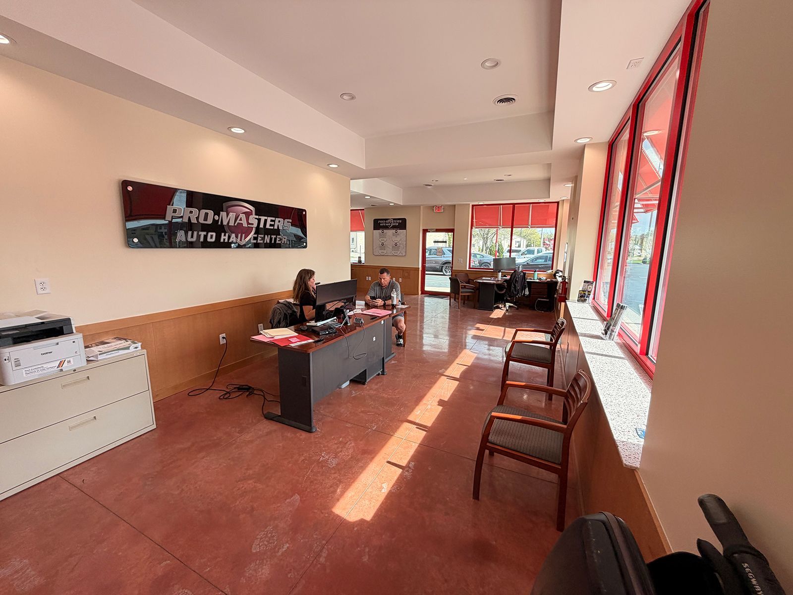 Bright lobby with reception desk, red chairs by large windows, and sunlight streaming across the floor.