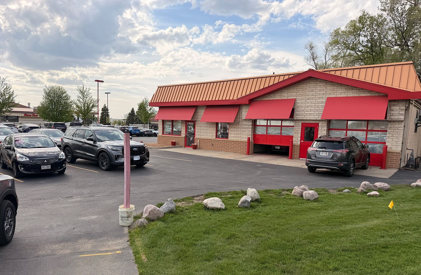 Fast-food restaurant with red awnings and parked cars in a strip mall parking lot
