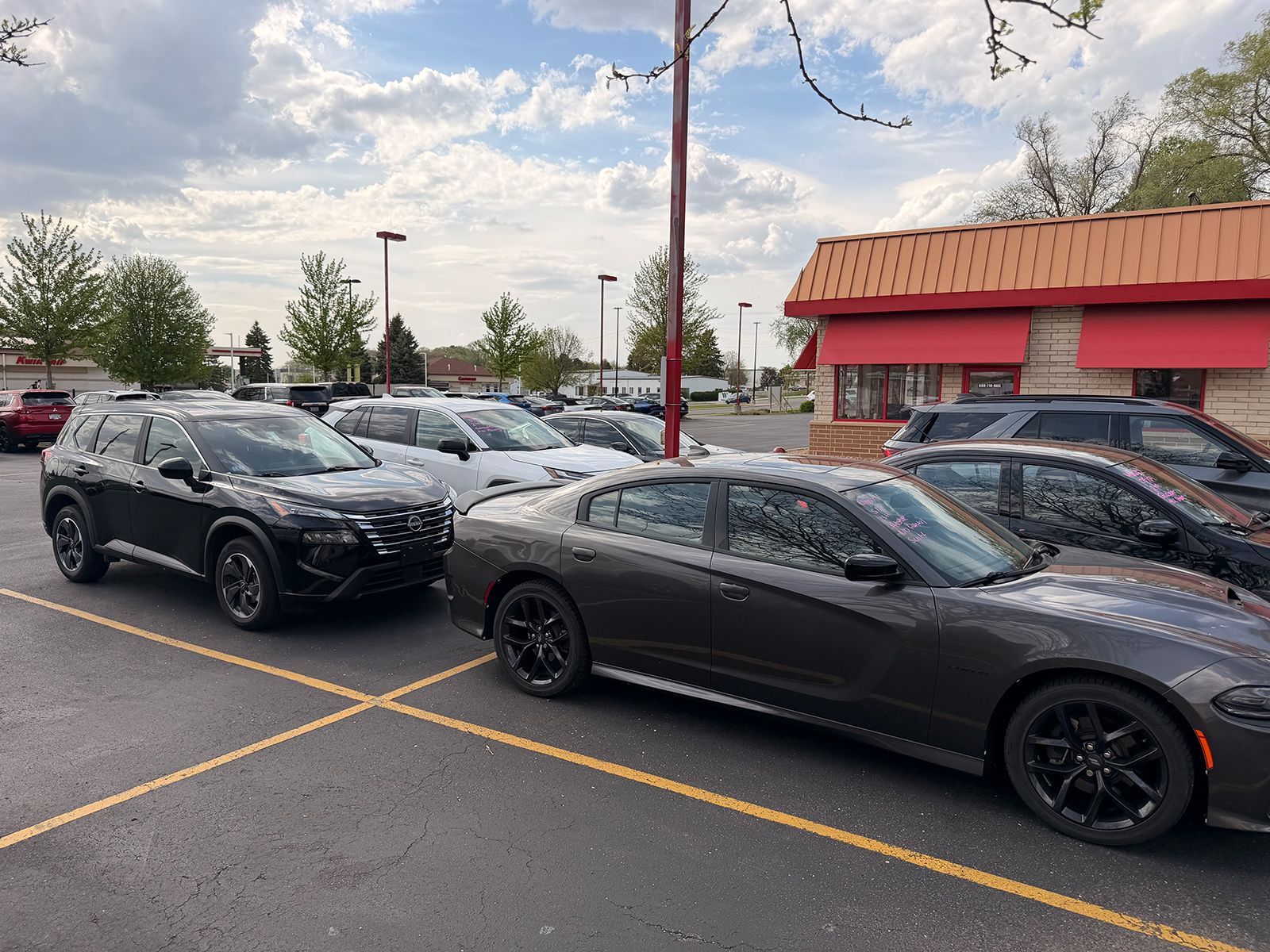 Black sports coupe parked in a lot beside a black SUV under cloudy skies.