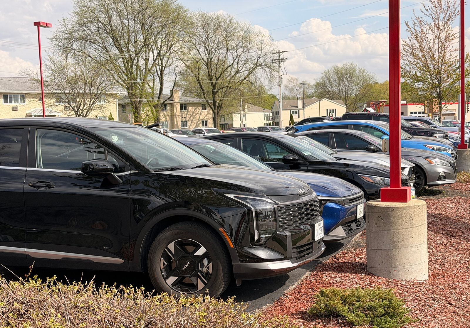 Black SUV parked in a lot beside red lamp posts and spring trees under a cloudy sky
