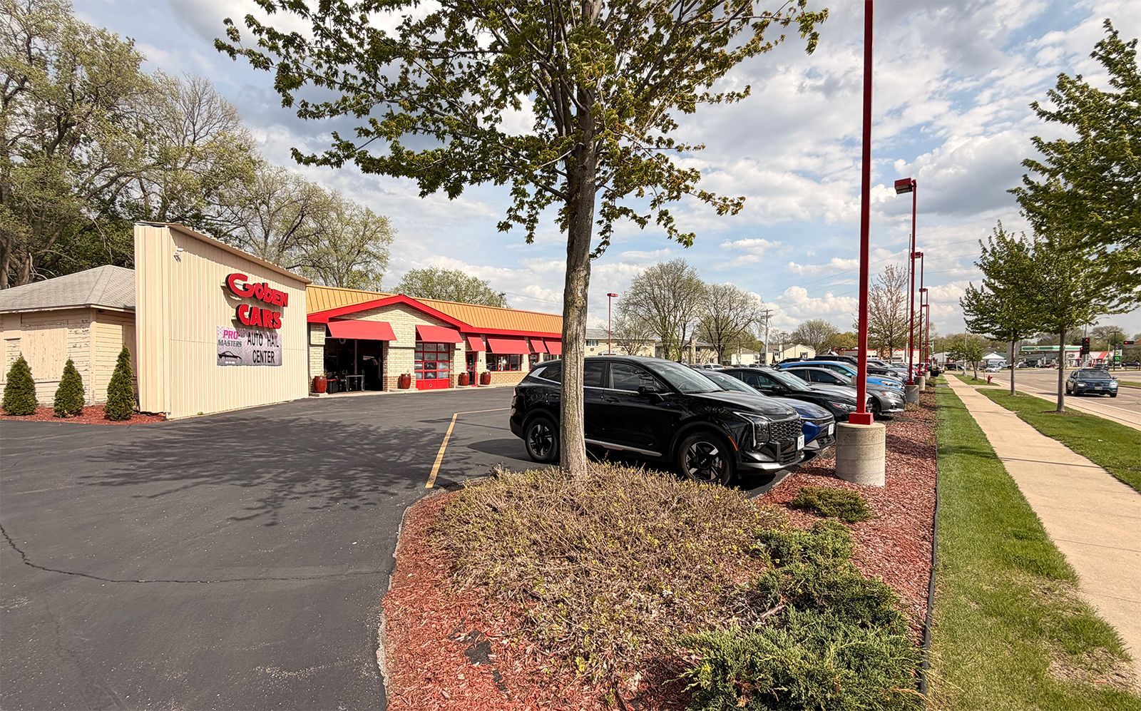 Restaurant storefront with red awnings, parked cars, and a sidewalk along a roadside under cloudy skies