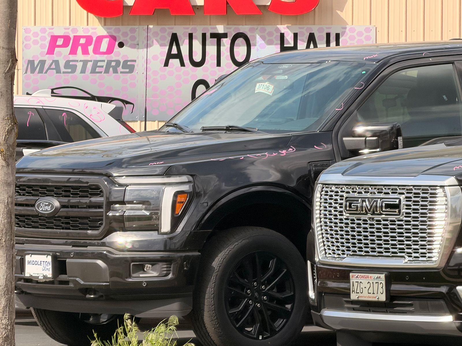 Black Ford truck parked beside a silver GMC at an auto junkyard sign.
