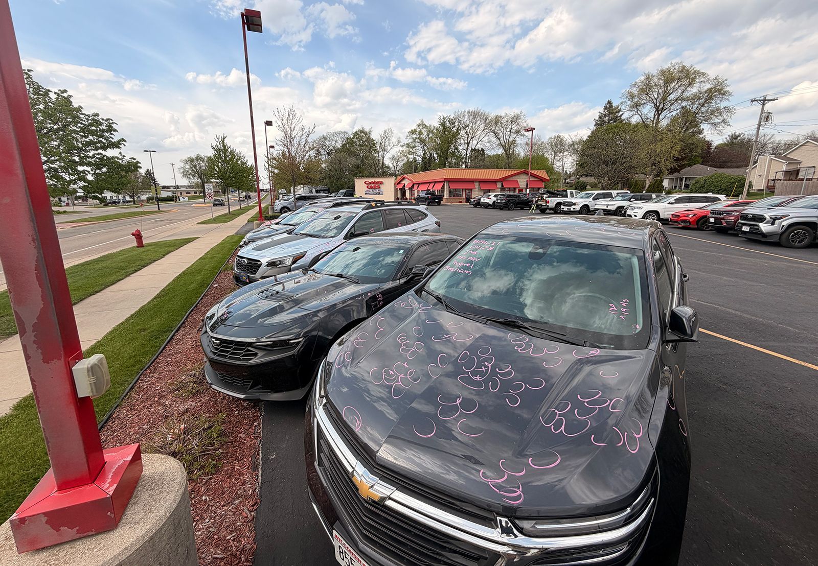 Row of parked cars in a dealership lot, with a black sedan in the foreground under a cloudy sky
