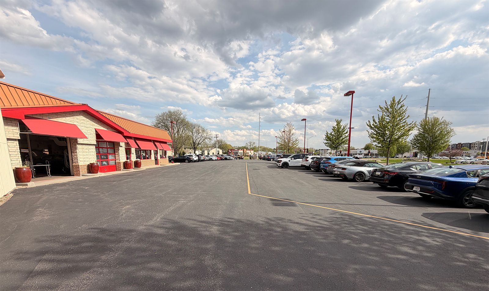 Parking lot beside a red-roofed store under a cloudy sky, with rows of parked cars and trees.