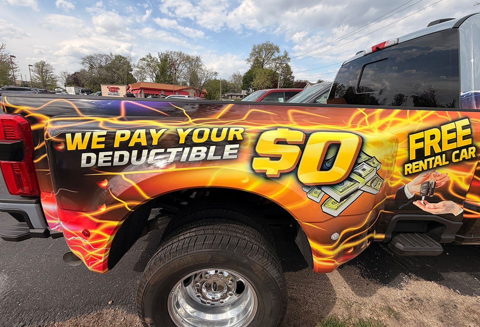 Branded pickup truck with fiery wrap advertising “We Pay Your Deductible $0” and “Free Rental Car”