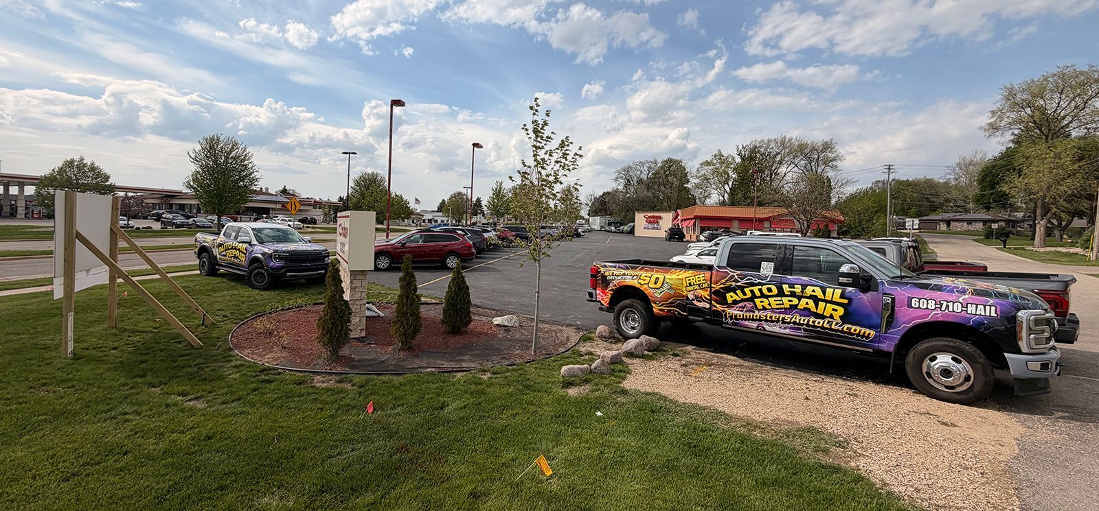 Colorfully wrapped pickup trucks parked at a grassy roadside lot under a partly cloudy sky