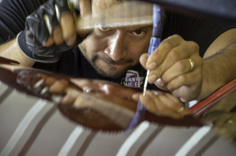 Man closely inspecting and sanding a glossy wooden surface with a tool