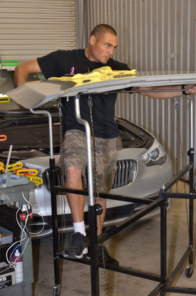 Man leaning over a metal workbench in a garage, working on a silver car body panel.