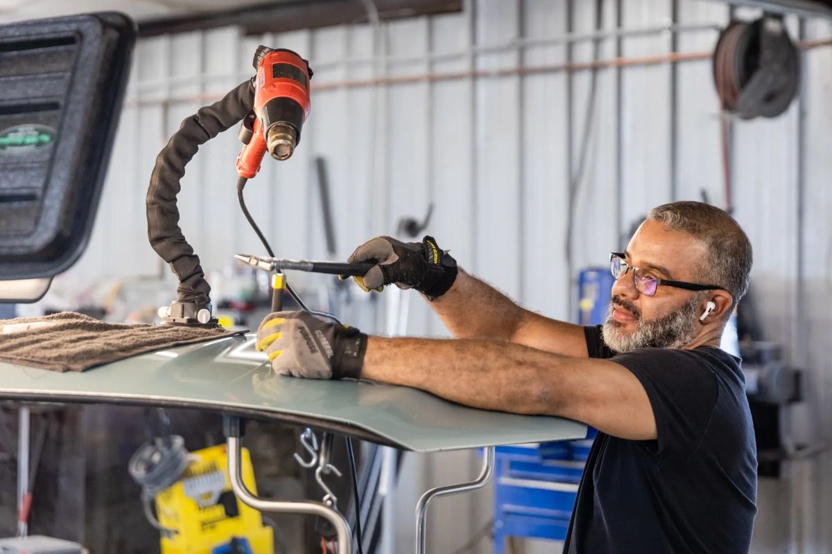 Worker welding on a car panel in a garage, wearing safety glasses and gloves