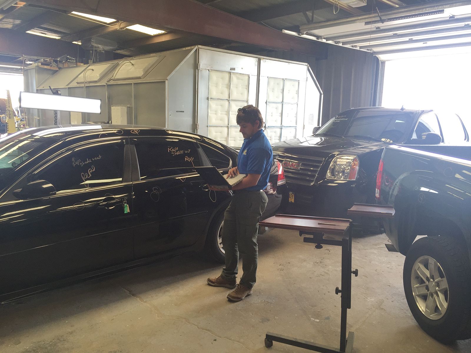 A man is standing in front of a black car in a garage.