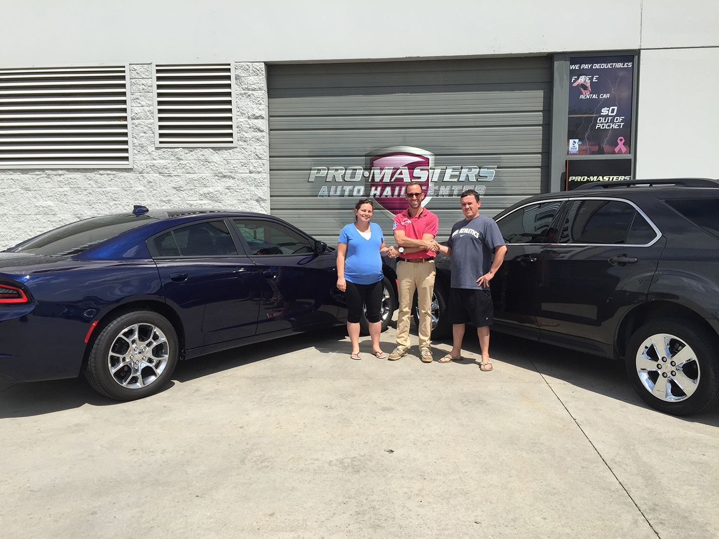 A group of people standing in front of two cars in a parking lot.