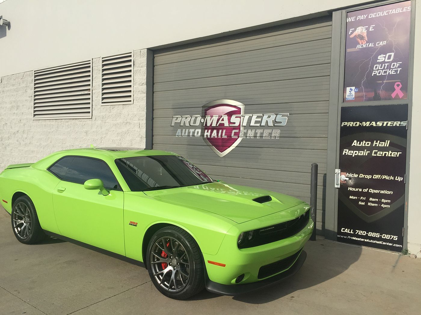 A green dodge challenger is parked in front of a garage door.
