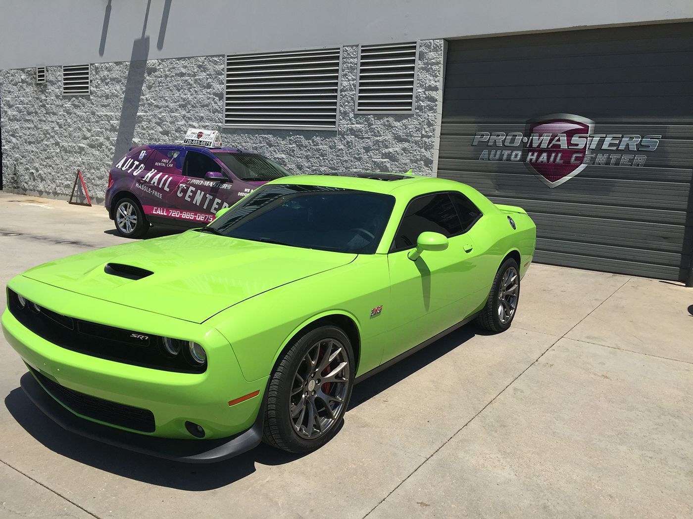 A green dodge challenger is parked in front of a building.