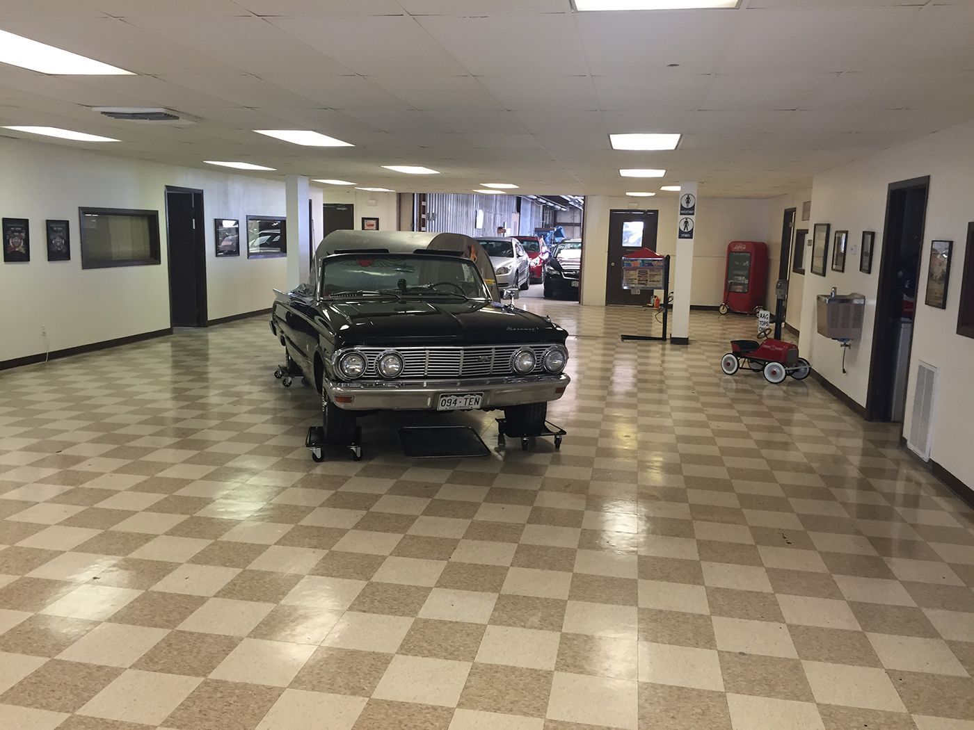 A car is parked in a large room with a checkered floor.