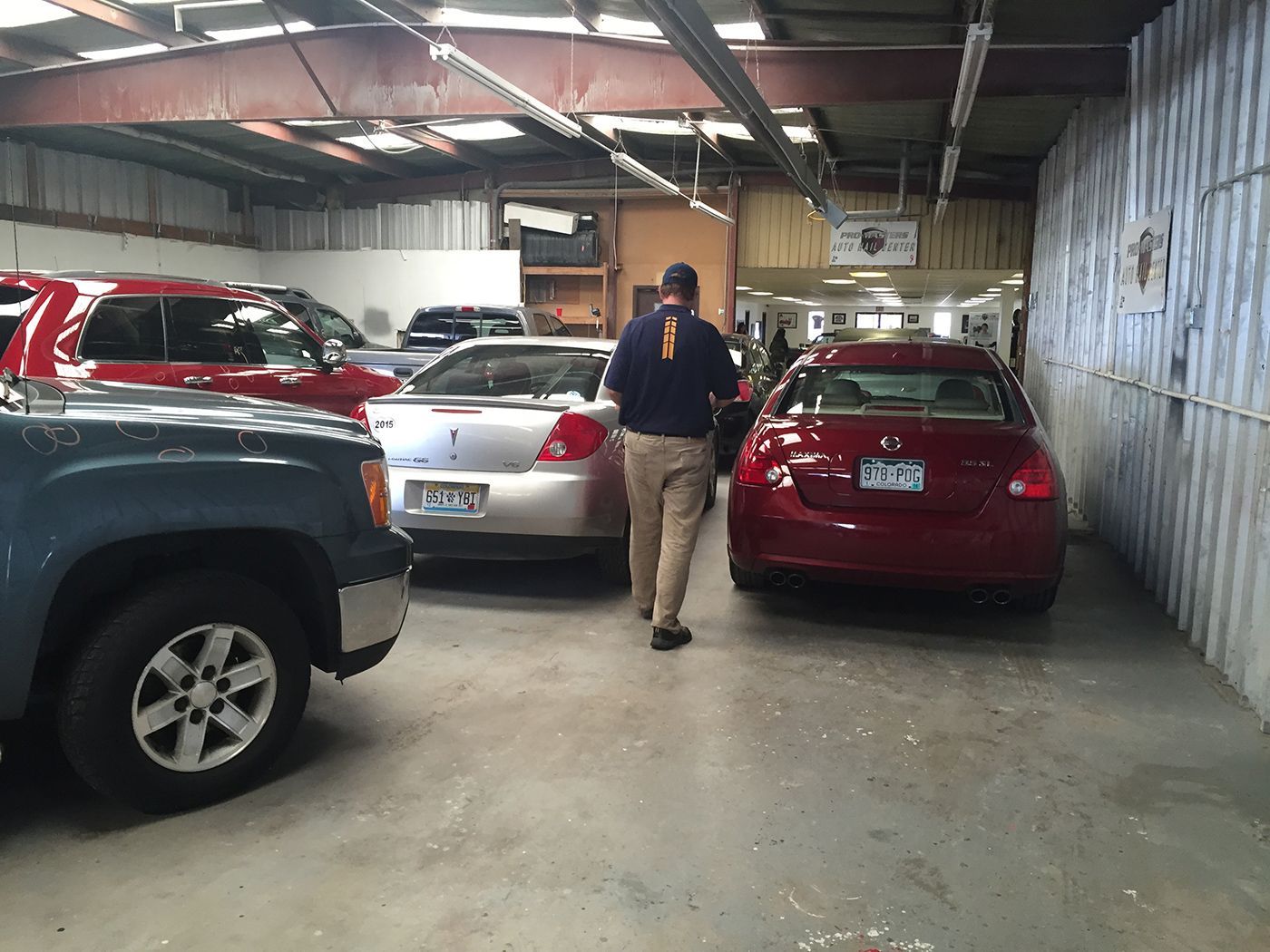 A man is standing in a garage looking at cars.