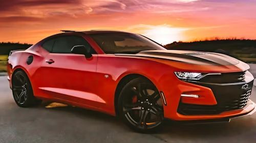Red sports car parked on a road at sunset with a dramatic orange sky