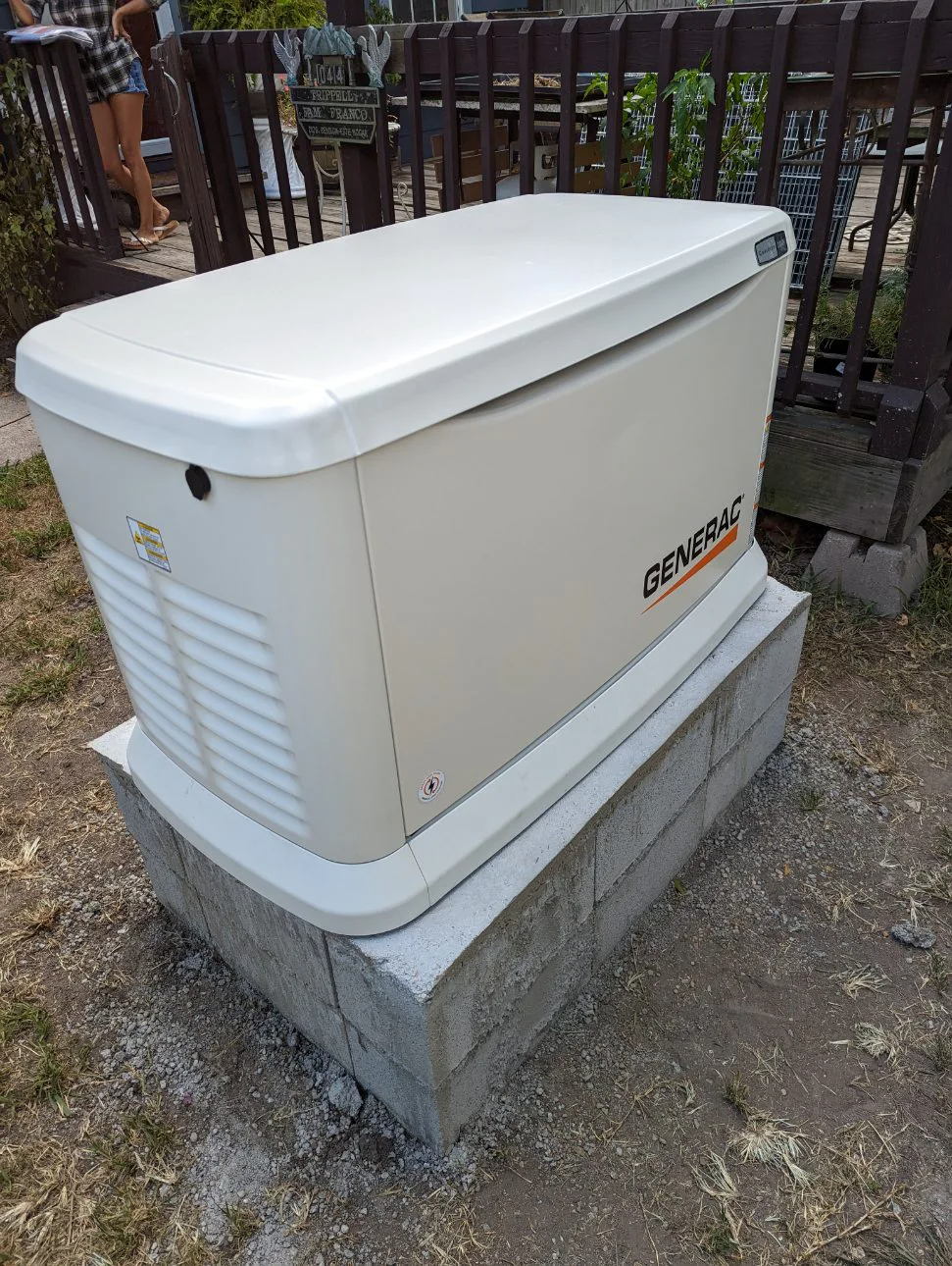 Tan Generac generator on concrete blocks, outdoors near a wooden fence.