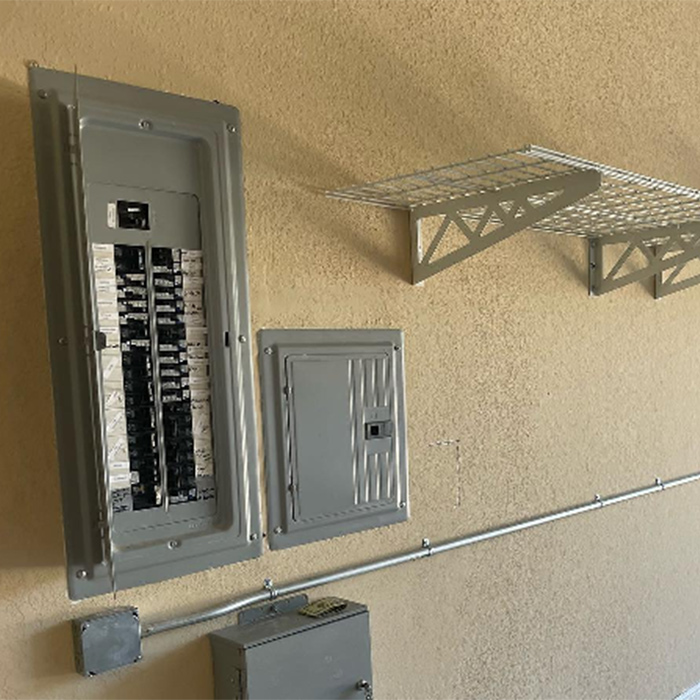 Electrical panel, metal box and conduit on a beige wall, with shelving above.