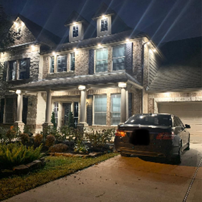 Night view of a two-story brick house with lit exterior lights. A car is parked in the driveway.