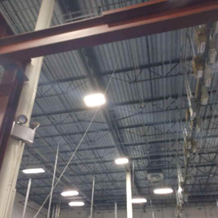 Warehouse interior: metal beams, overhead lighting, corrugated ceiling, and hanging equipment.