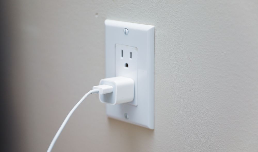 White wall outlet with a white phone charger plugged in.
