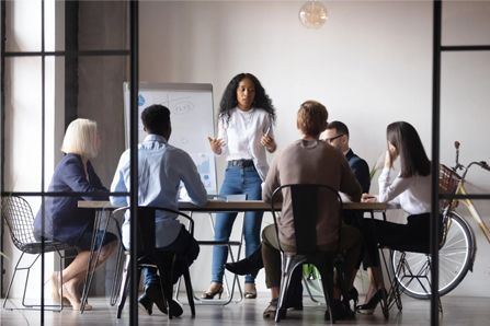 A Black woman presents to a diverse group in an office setting.