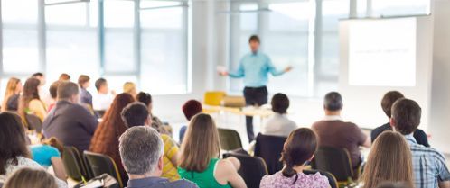 A man presenting to a seated audience in a conference room. 