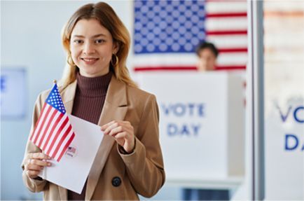 Woman at a polling place holding a small American flag and ballot, smiling. 