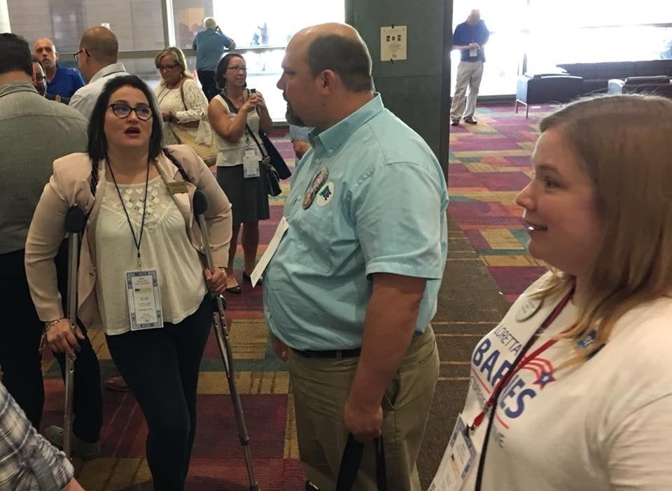 A woman with crutches talks to a man in a light blue shirt.