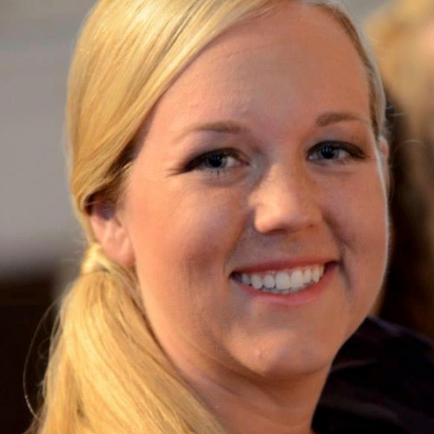 A woman with long blonde hair is smiling and wearing a purple shirt.
