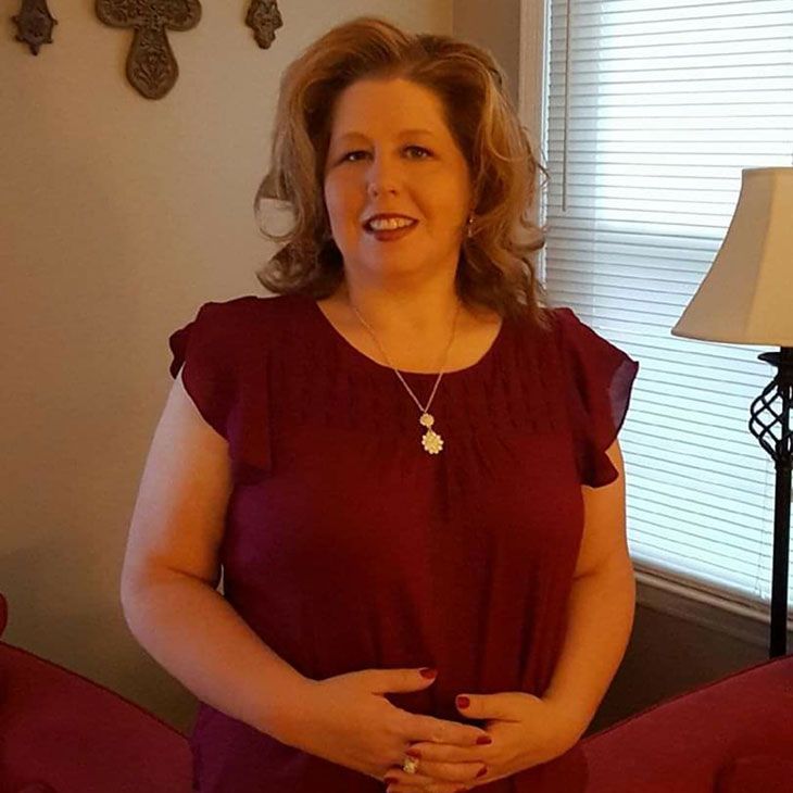 A woman in a red shirt is standing in front of a lamp