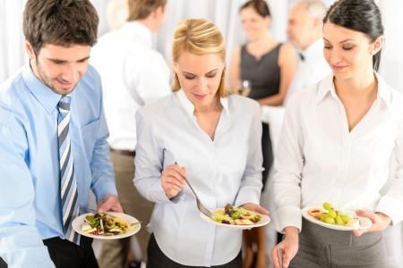 Three office workers holding plates of salad at a workplace lunch buffet
