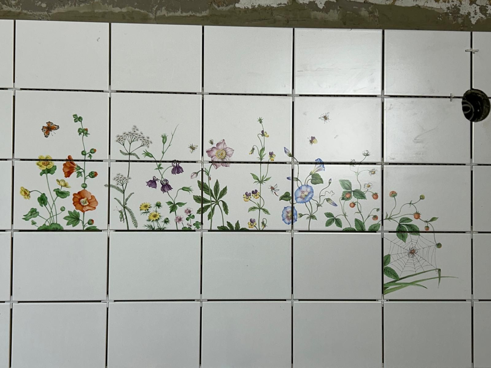 Dekoratives Fliesenband aus weißen Wandfliesen mit handgemalten Blumen- und Pflanzenmotiven – individuelle Fliesenarbeit 