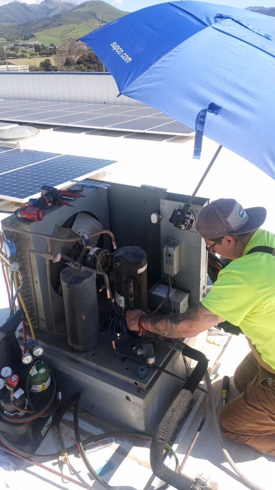 A man is working on a machine on a roof under an umbrella.