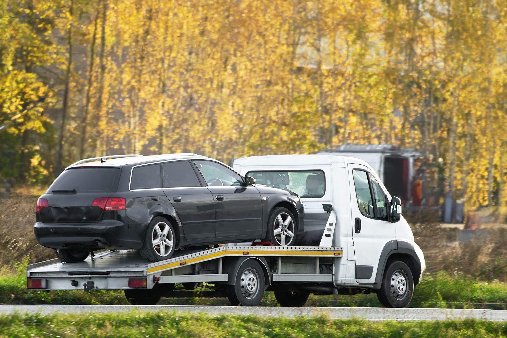 A tow truck is carrying a black car on the back of it.