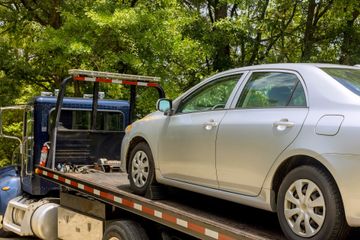 A silver car is being towed by a tow truck.