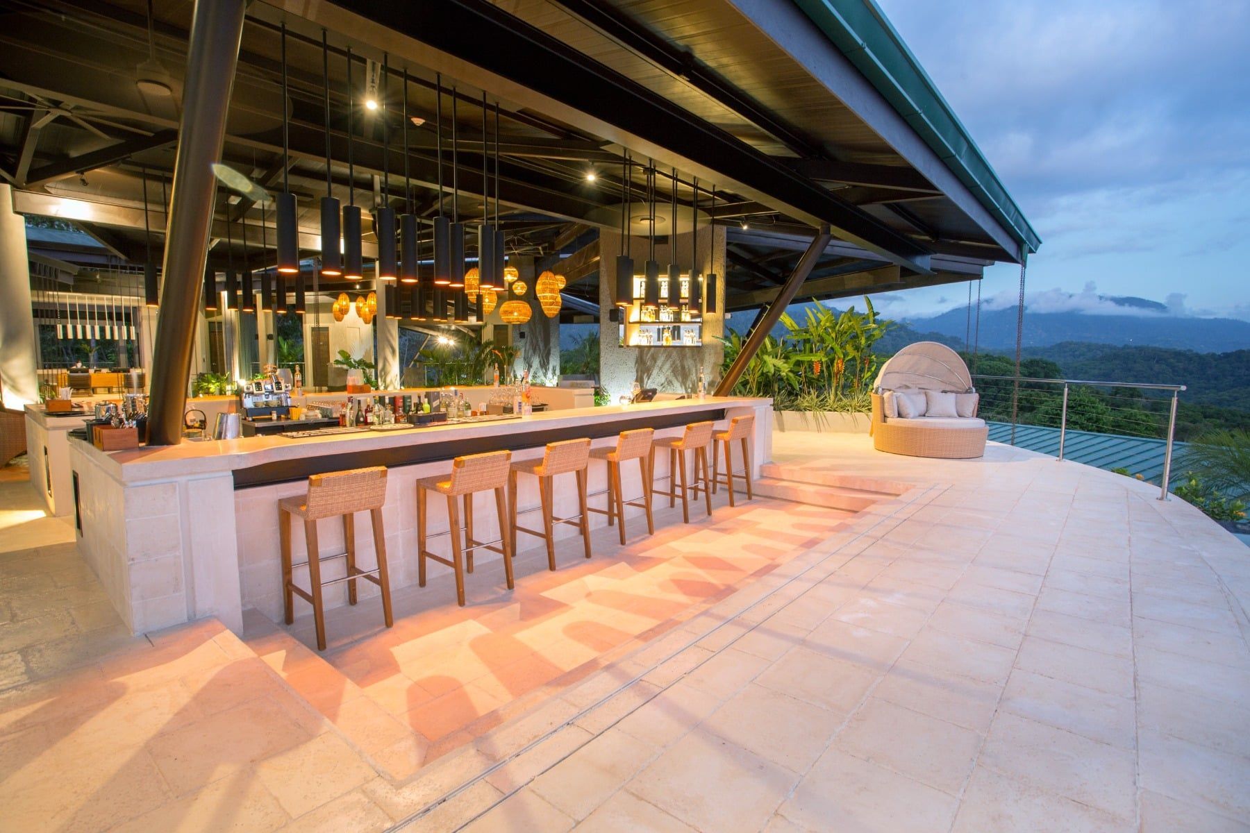 A restaurant with a long bar and stools on a balcony overlooking the mountains.