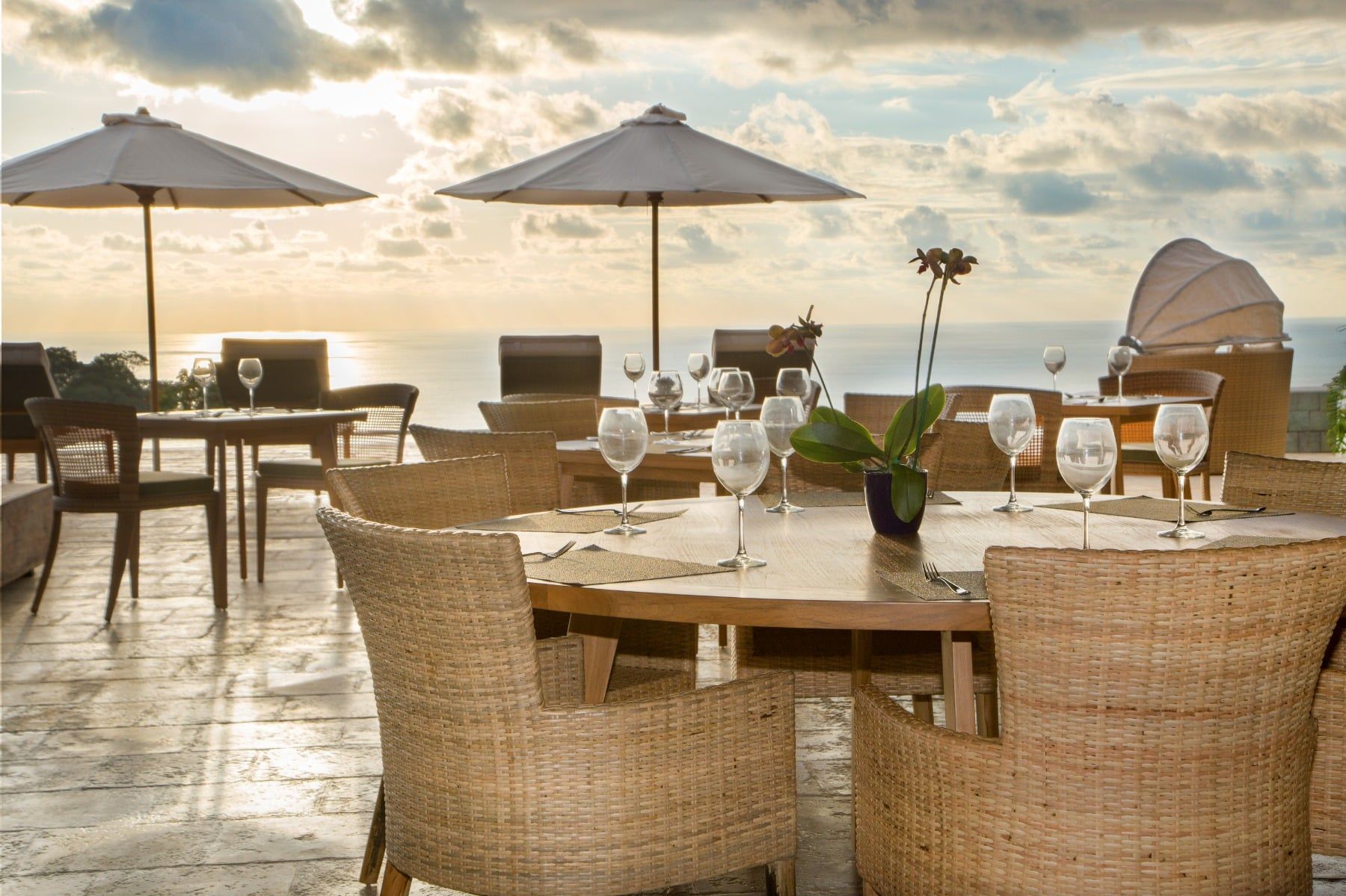 A restaurant with tables and chairs and umbrellas overlooking the ocean.