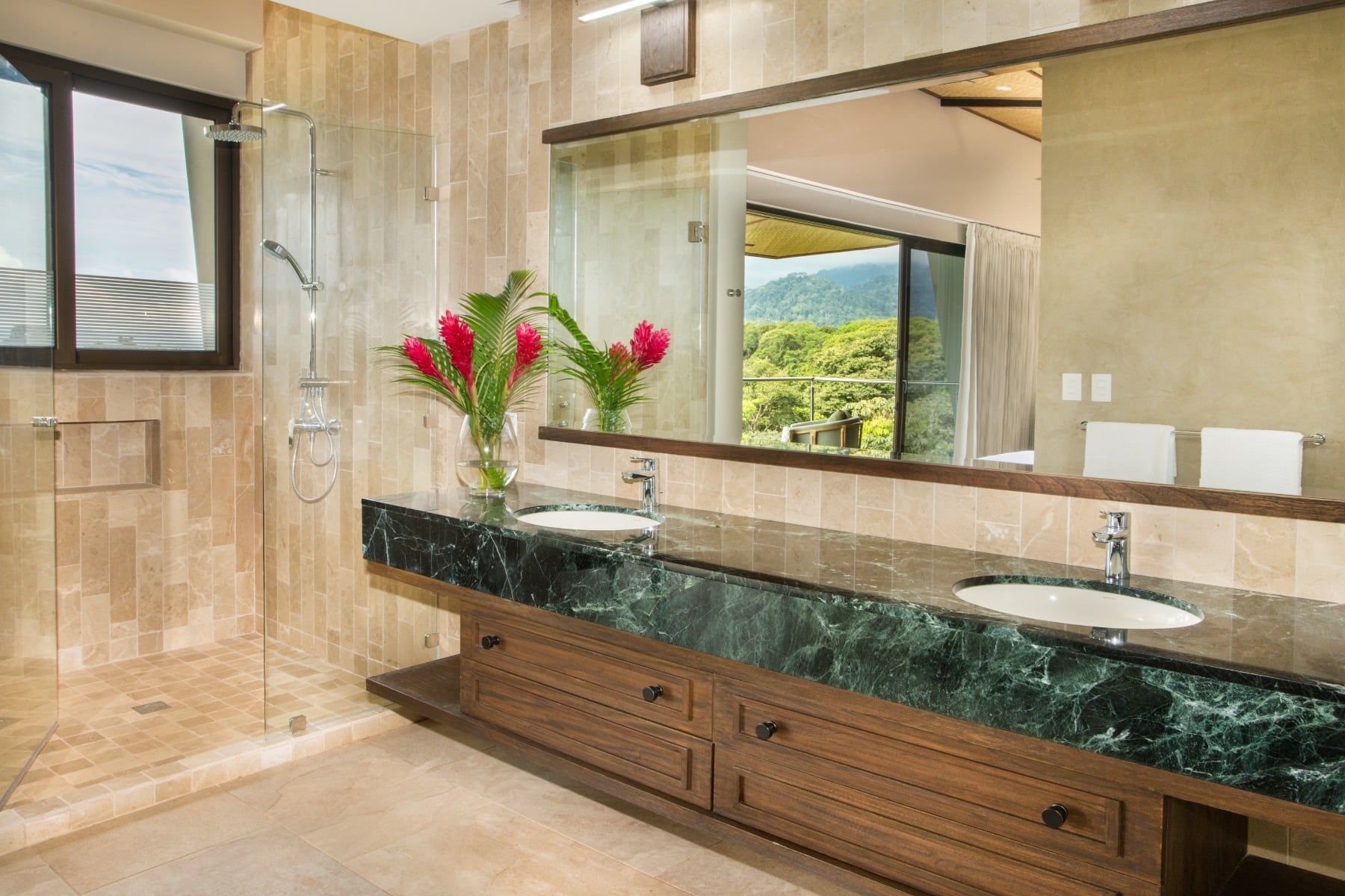 A bathroom with two sinks , a large mirror and a walk in shower.