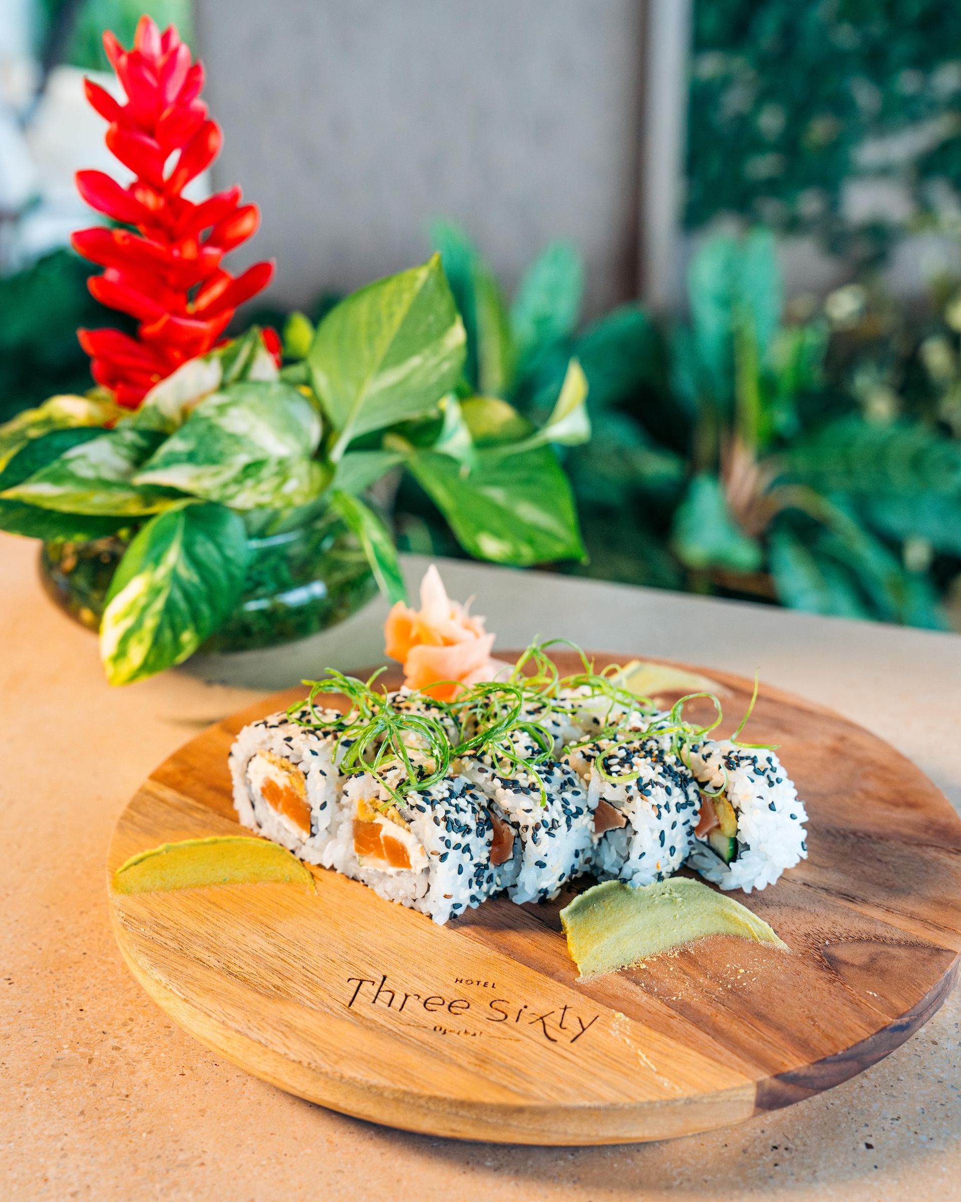 A wooden cutting board with sushi on it and a plant in the background.