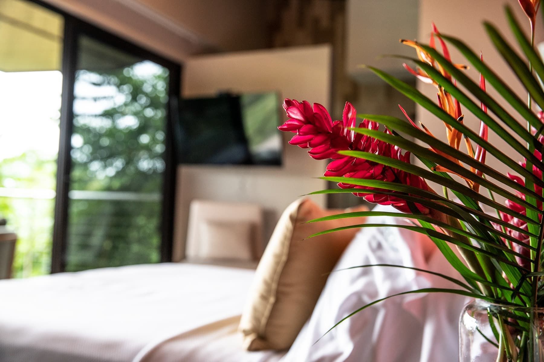 A vase of flowers is sitting on a bed in a hotel room.